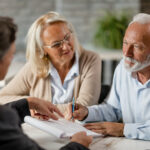 Senior couple signing a contract while having a meeting with ins
