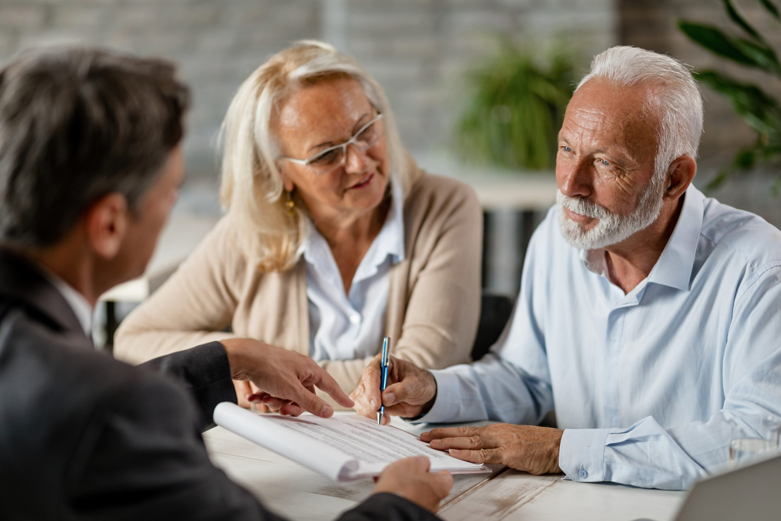 Senior couple signing a contract while having a meeting with ins